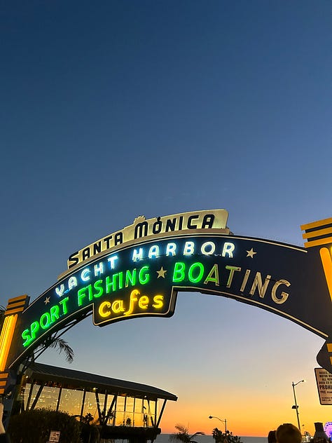 the pier sign, the pacific park sign, the end of route 66 sign, and the sun setting and rising over the pier