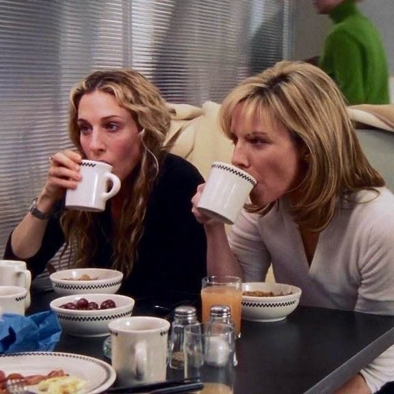 This may contain: two women sitting at a table drinking from mugs with food in front of them