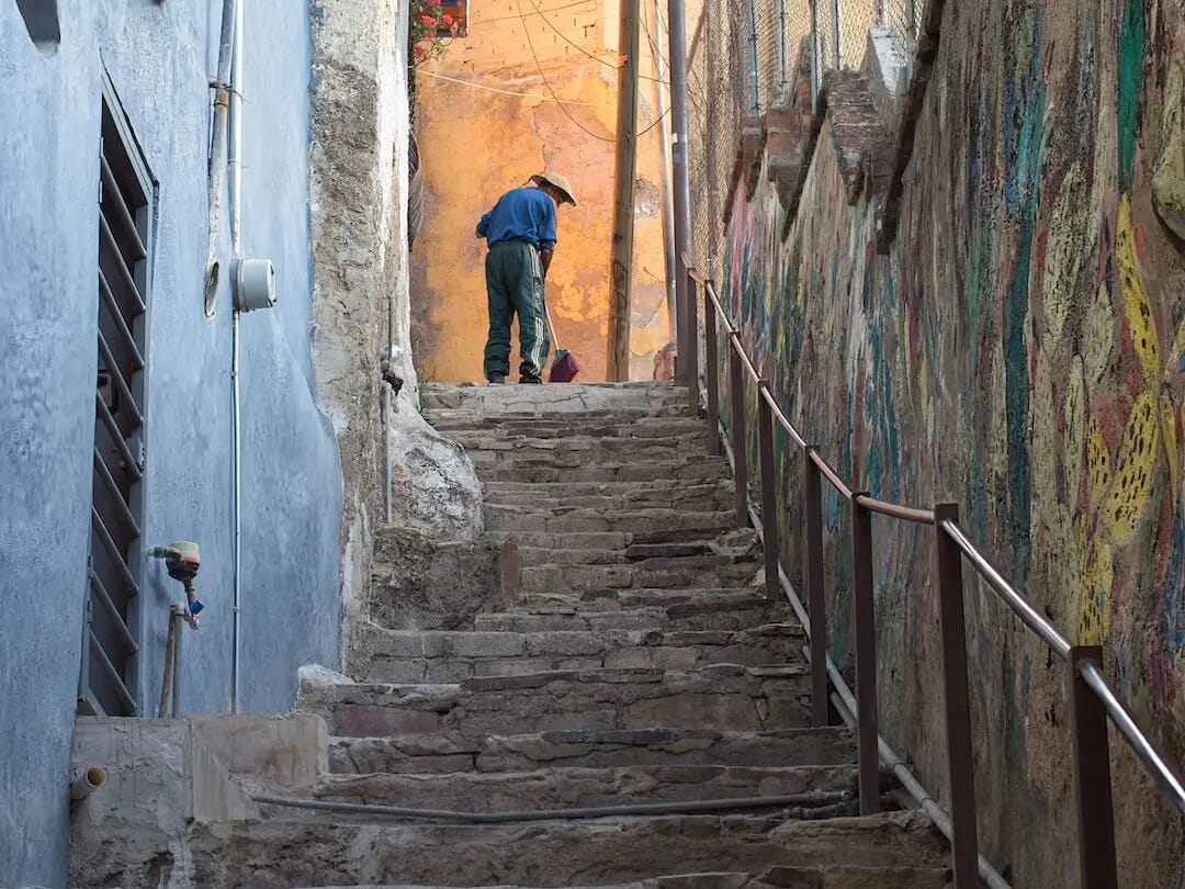 A stepped alleyway with graffiti on one wall and a man brushing at the top 