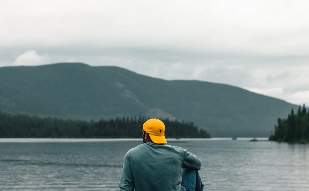 a person standing in front of a body of water with trees and hills in the background a person standing in front of a body of water with trees and hills in the background