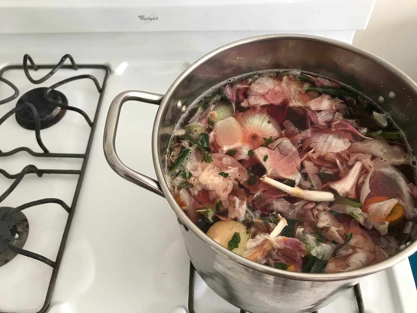 silver metal pot full of vegetable scraps on a white stovetop