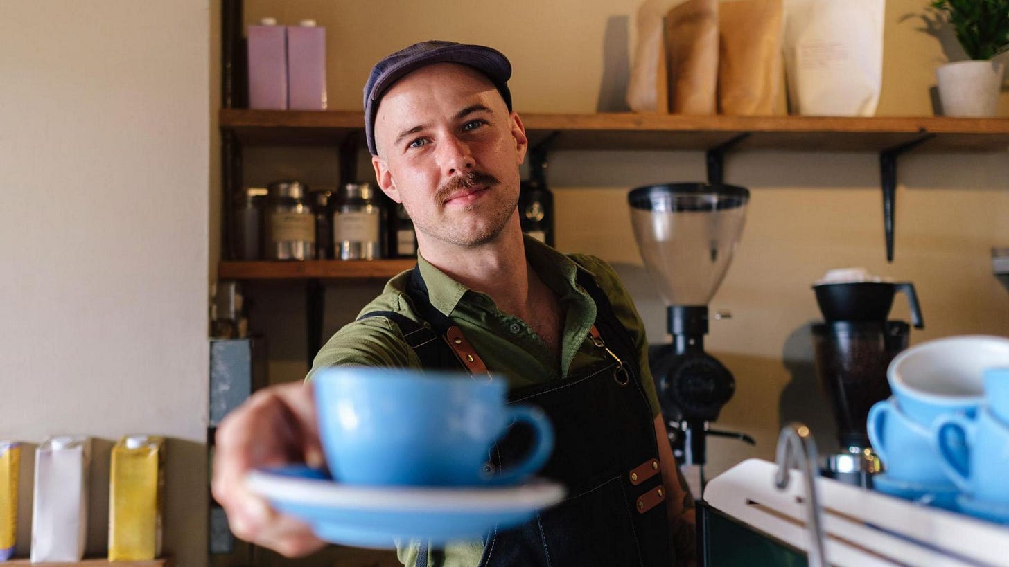 A barista extends a freshly brewed cup of coffee to the camera A barista extends a freshly brewed cup of coffee to the camera