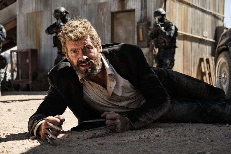 An injured Logan lies on the ground with his adamantium claws extended as armed soldiers surround him. An injured Logan lies on the ground with his adamantium claws extended as armed soldiers surround him.