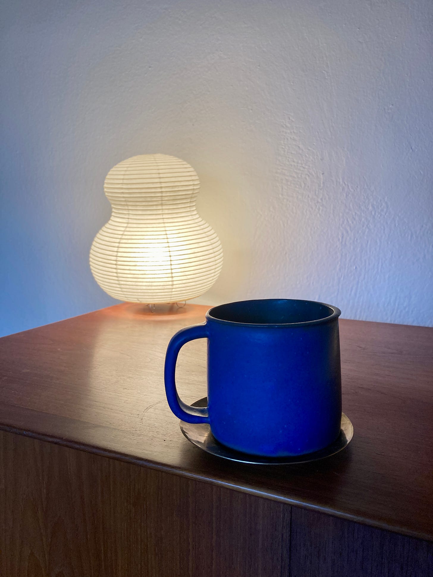 Image of a bright blue mug on a wooden credenza. A small paper lamp shines in the background.