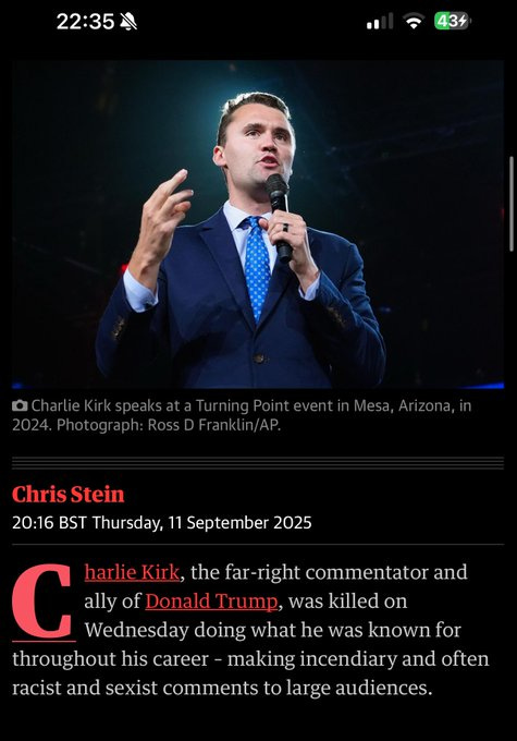 Charlie Kirk speaking on stage, wearing a blue suit and tie, holding a microphone in one hand, gesturing with the other. A dark background is visible behind him. Text overlay includes "Charlie Kirk speaks at a Turning Point event in Mesa, Arizona, in 2024. Photograph: Ross D Franklin/AP."