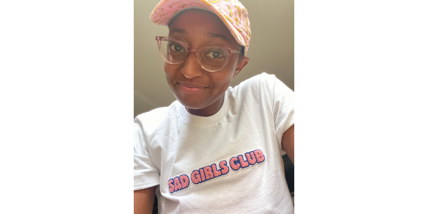 Ashley wearing a pink banana cap, pink sunglasses, and a t-shirt that says "SAD GIRLS CLUB"