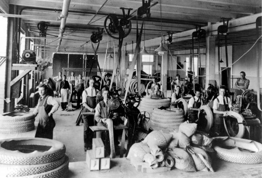 Old black and white photo of workers in aprons at machines making tires Old black and white photo of workers in aprons at machines making tires