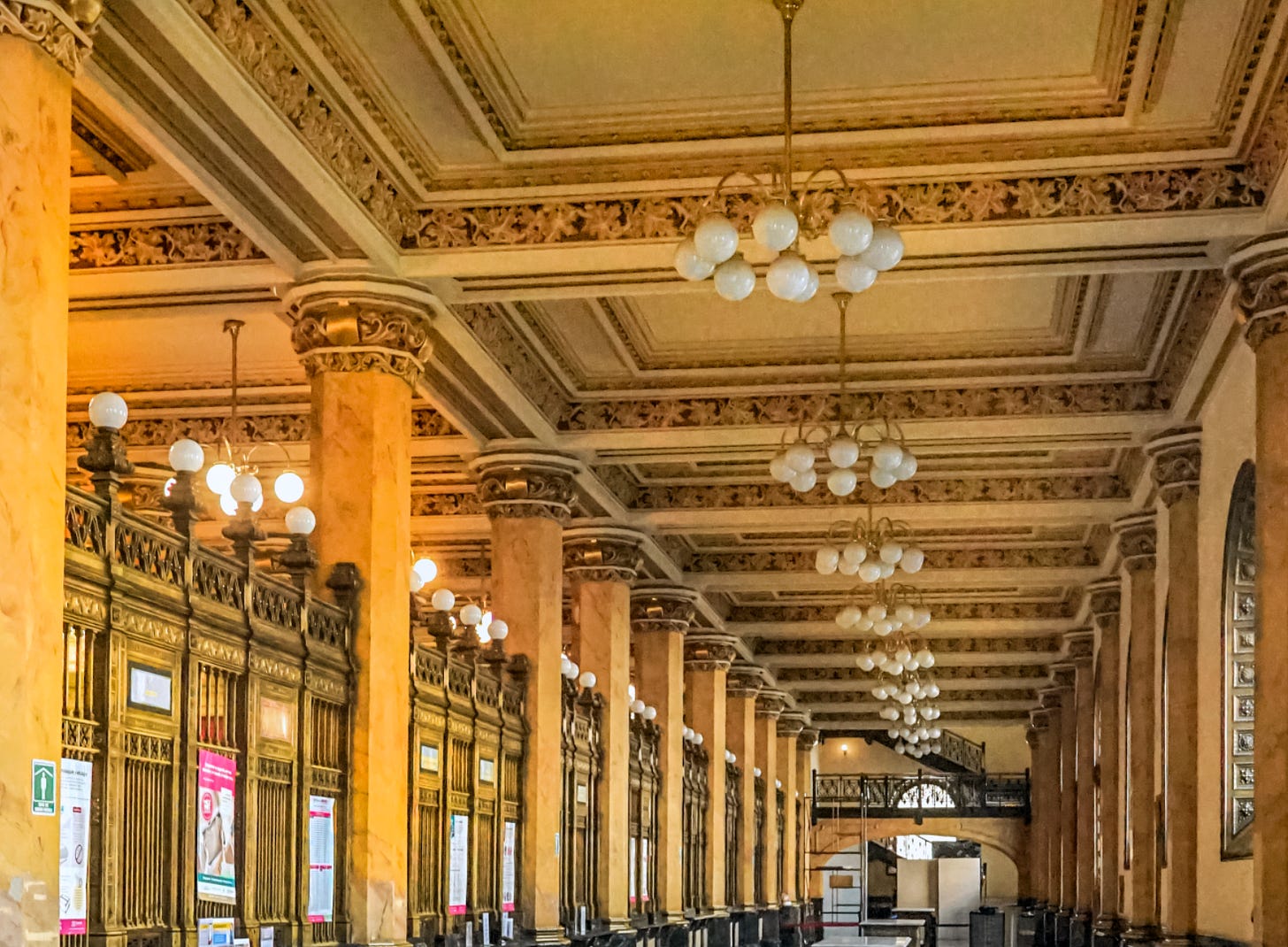 Golden interior of Mexico city Postal Palace with columns light fixtures and ornate carvings on the ceiling.