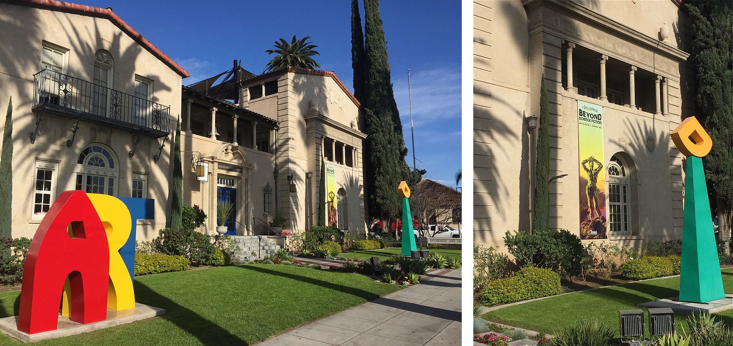 LEFT: Angled photo of the Riverside Art Museum with the spiky shadow of a palm tree falling on the building facade. In primary colors, the letters A, R, and T overlap in sculpture  RIGHT: Closer photo of the banner for "Beyond Science Fiction" featuring the robot Giskard from ROBOTS OF DAWN.