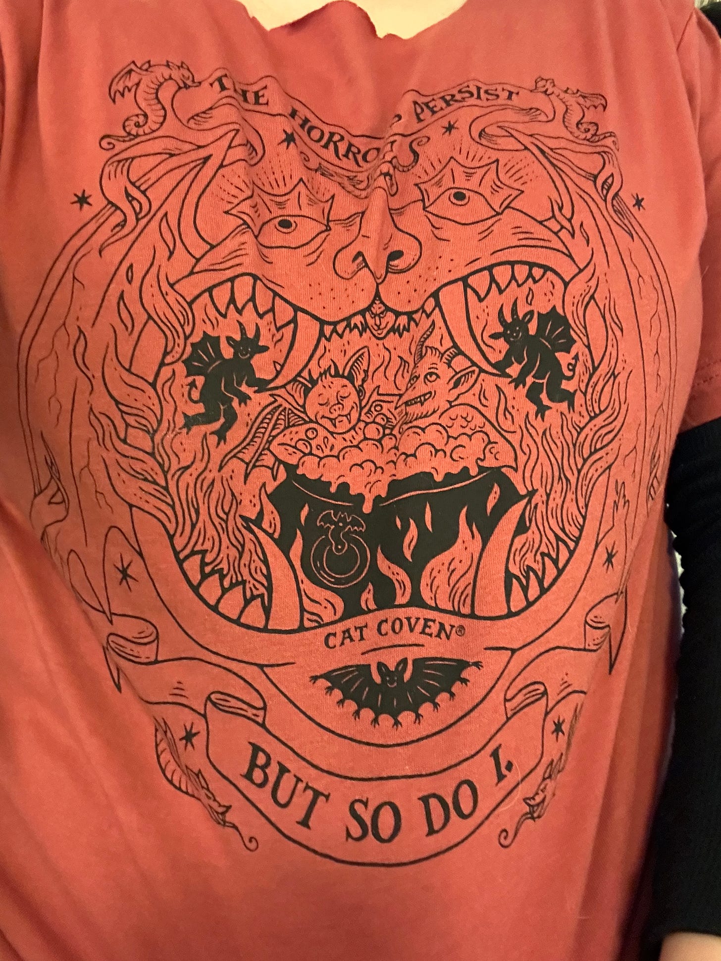 An autumnal orange t-shirt with a design depicting happy creatures in a bubbling cauldron with the whole tableau in the mouth of a monster. 
