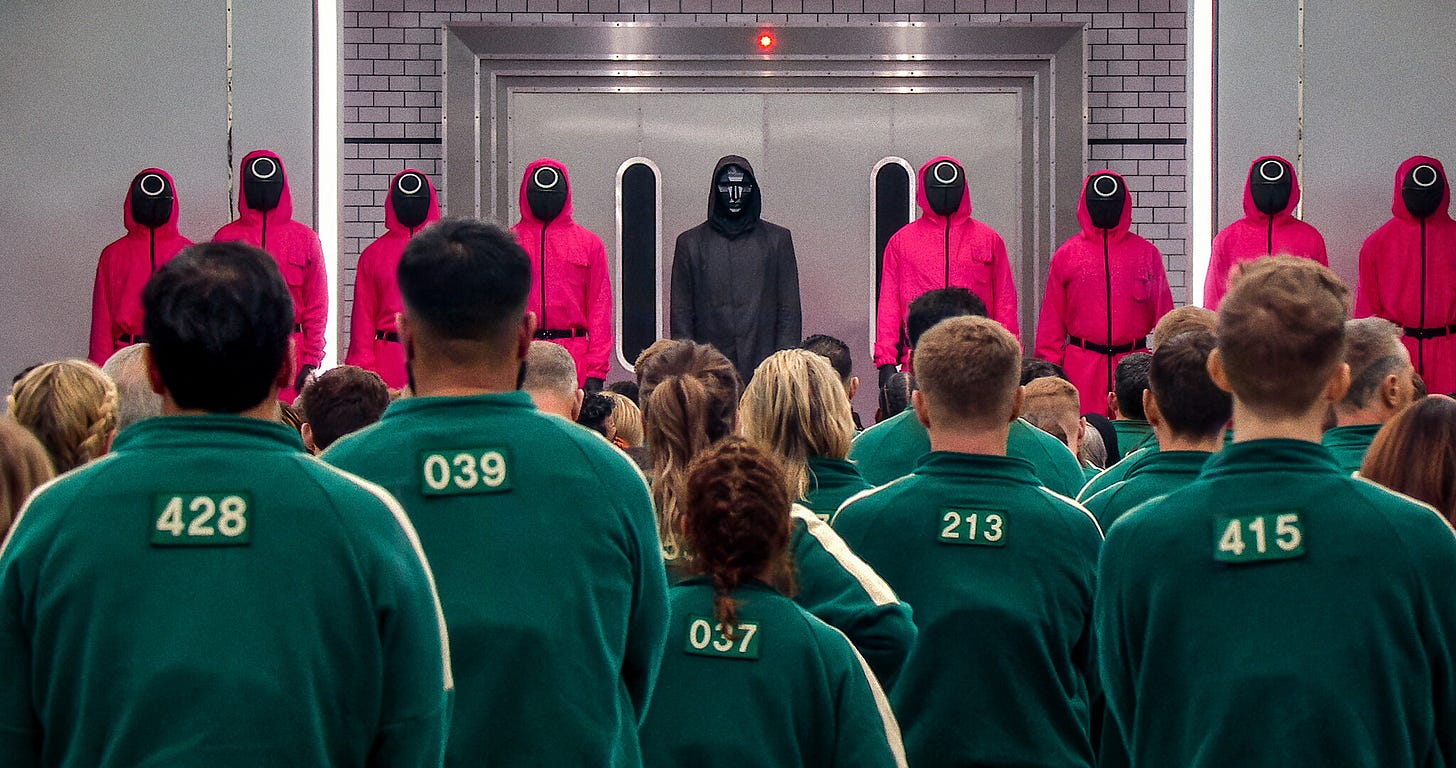 Squid Game: The Challenge - The Pink Guards and The First Man standing at the front while looking at a batch of new contestants. 