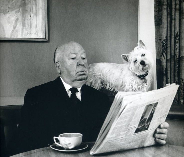 This may contain: a man sitting at a table reading a newspaper with a dog standing on his back