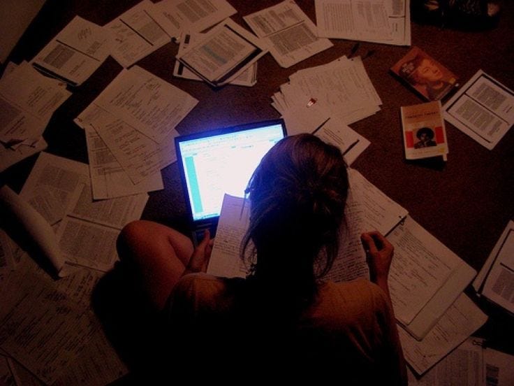This may contain: a woman sitting in front of a laptop computer surrounded by papers on the floor,