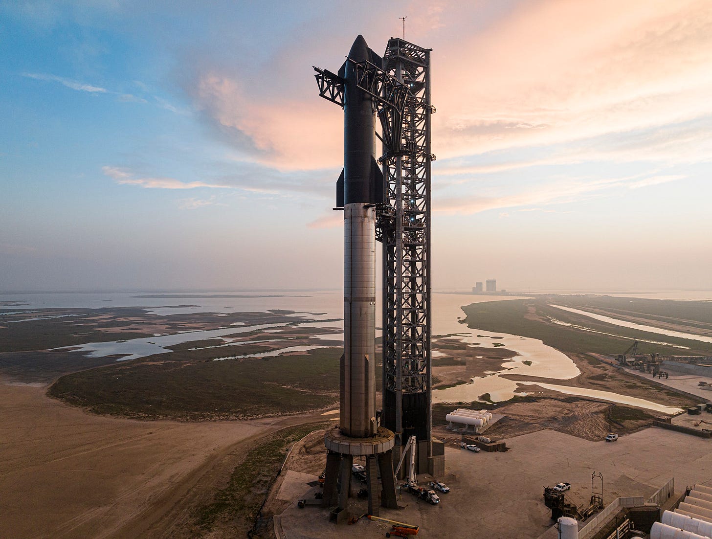 A black and silver rocket stacked alongside a large tower, on top of the version 1 launch mount in coastal Texas.