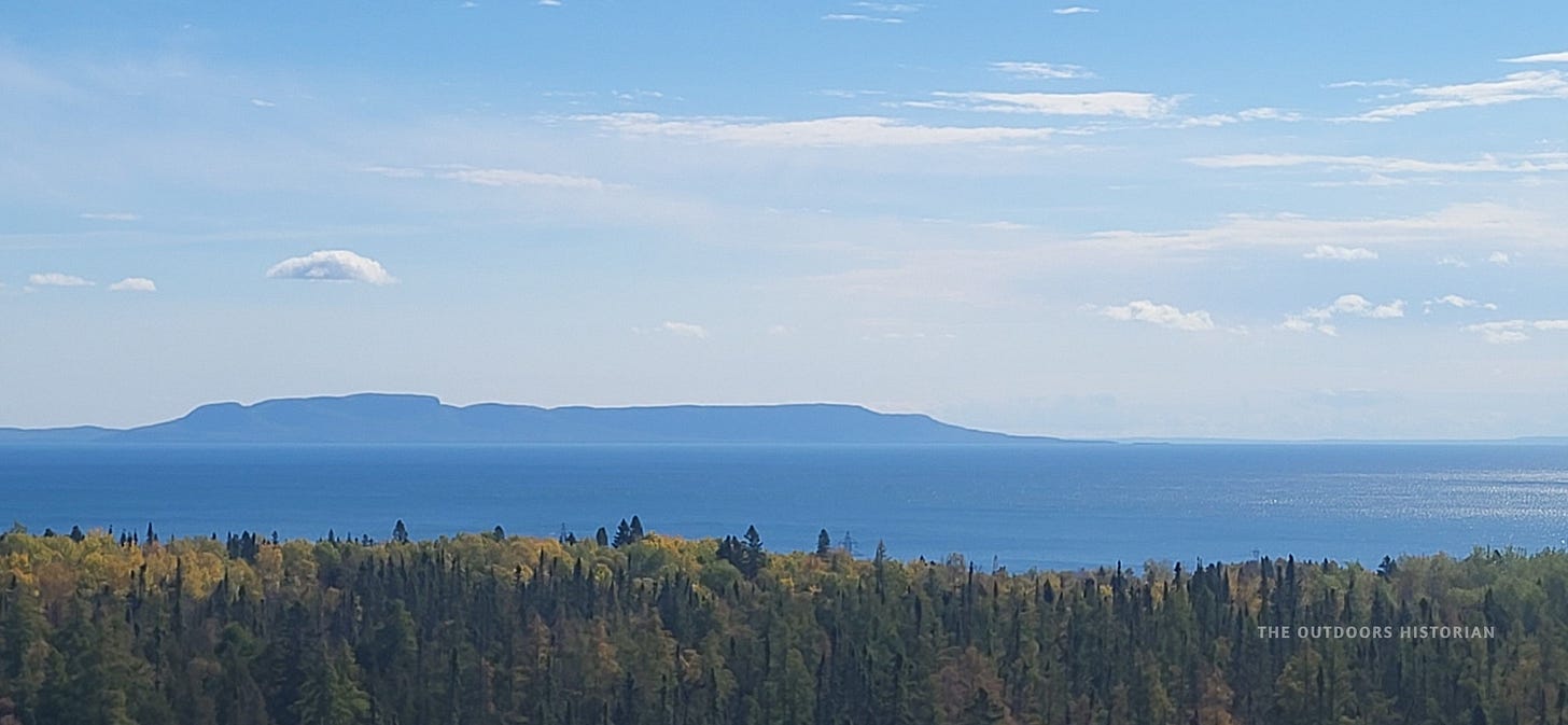 A landscape view across a bay of Lake Superior, featuring a long, rugged peninsula with rock formations that resemble a giant figure lying on its back.