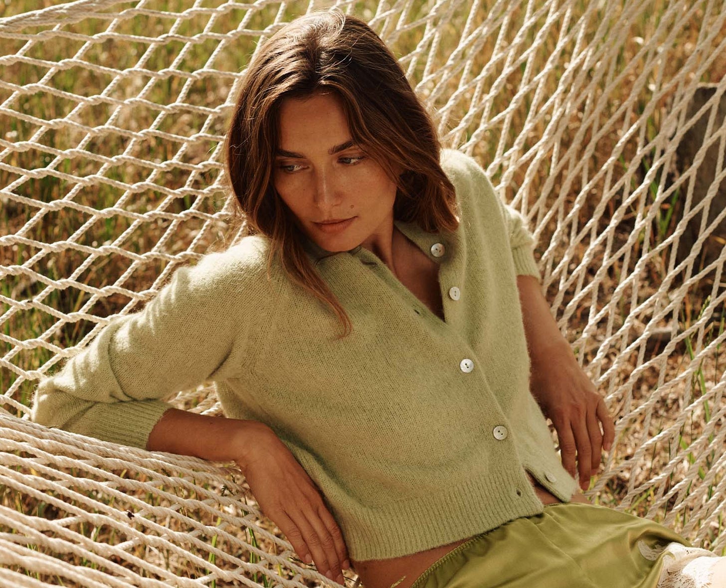 Woman in a green cardigan and shorts sitting in a hammock outdoors. 1