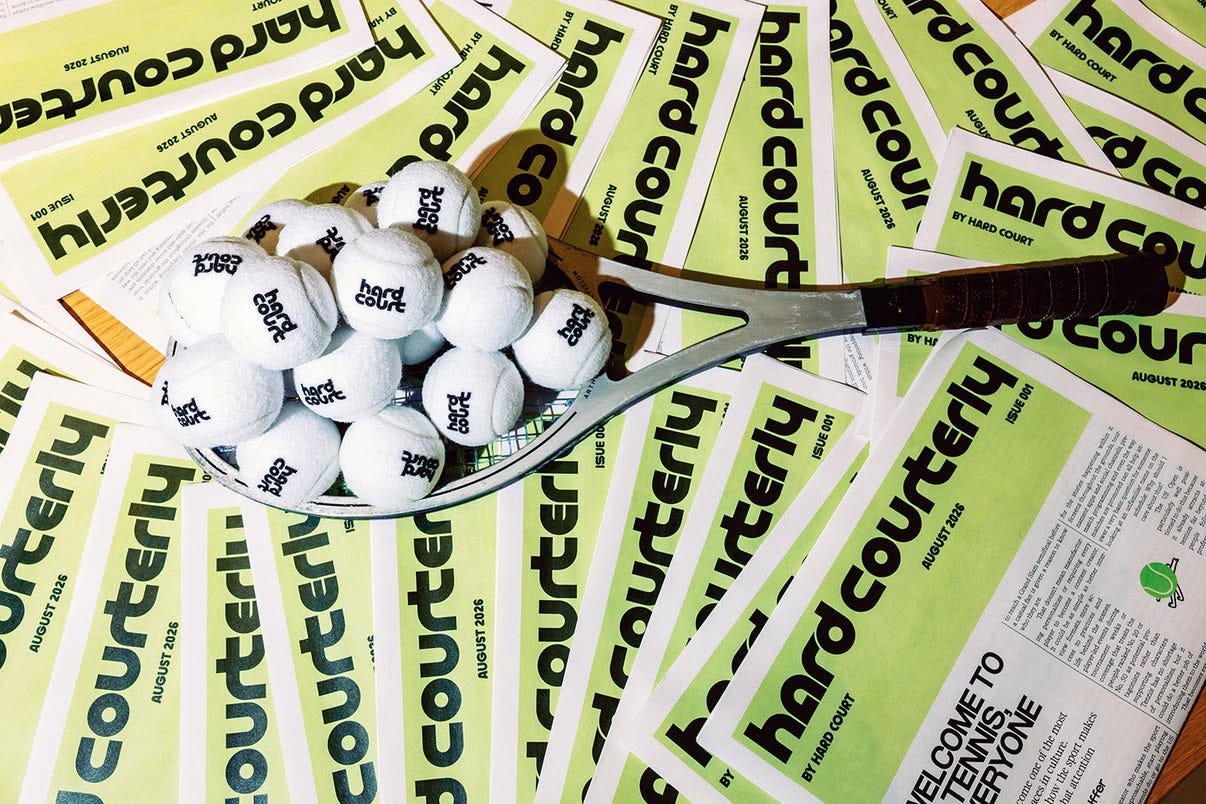 A tennis racquet resting across printed Hard Court editions beside a basket of white tennis balls. A tennis racquet resting across printed Hard Court editions beside a basket of white tennis balls.
