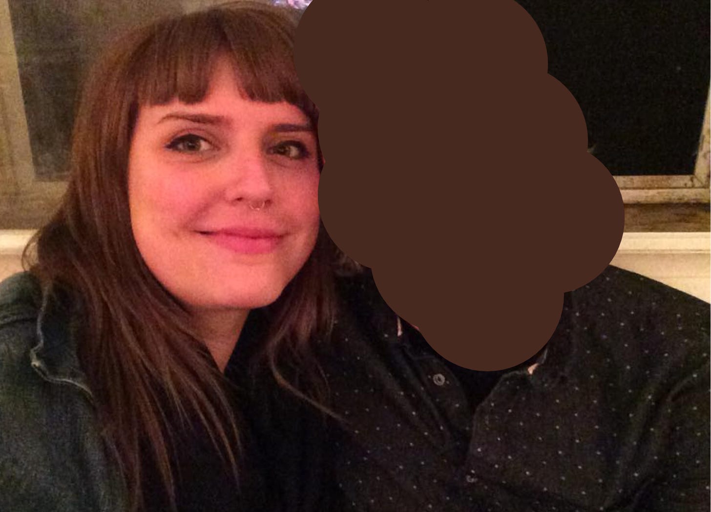 Image: Alej on left with brown hair, short bangs, smiling at the camera, with a man to their right whose face has been obscured by dark circles, he is wearing a dark button down shirt.