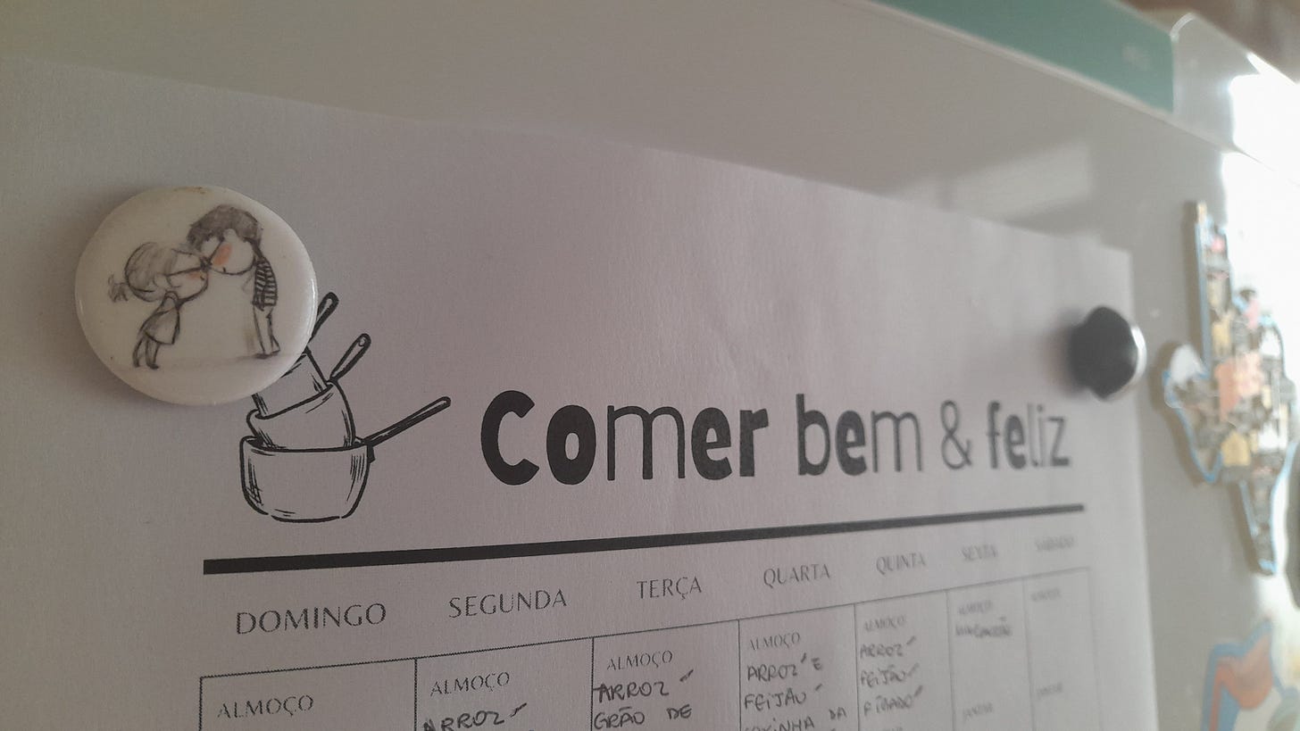 Planejador de refeições com o desenho de três panelas sobrepostas à esquerda do título "Comer bem & feliz". Também à esquerda um pequeno imã de geladeira com uma menina e um menino tocando as testas enquanto se olham. Planejador de refeições com o desenho de três panelas sobrepostas à esquerda do título "Comer bem & feliz". Também à esquerda um pequeno imã de geladeira com uma menina e um menino tocando as testas enquanto se olham.