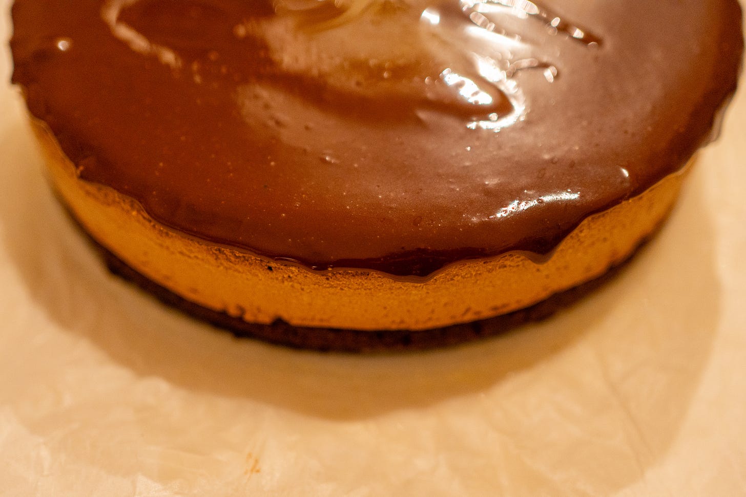 A whole round flourless chocolate espresso cake featuring a thick layer of lighter brown mousse topped with a glossy, dark chocolate mirror glaze.