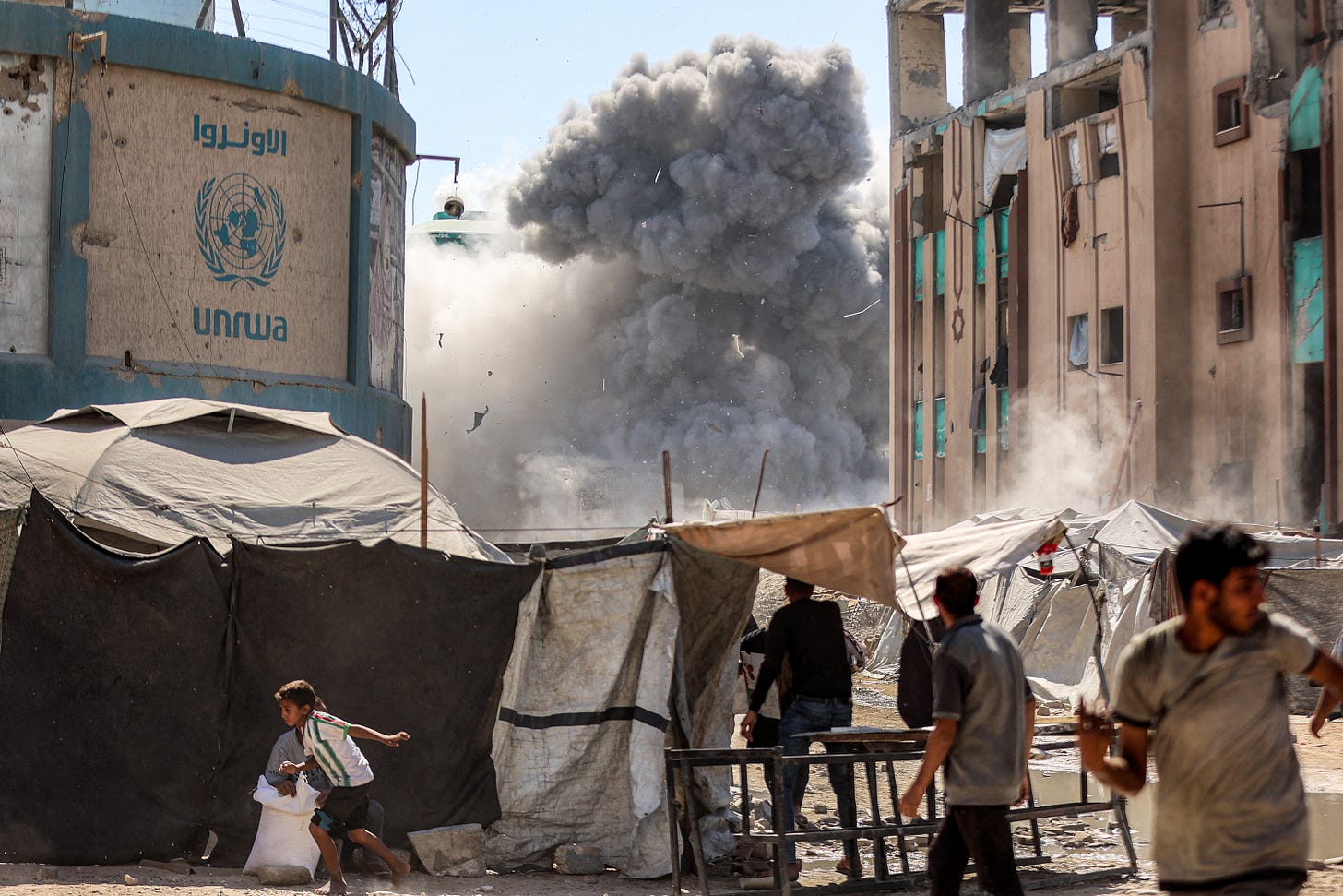 People running to take cover under tents, as an dust from a large explosion from an Israeli air strike rises in the background.