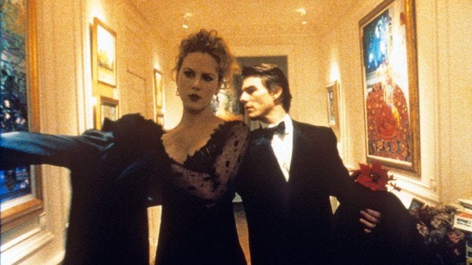 Nicole Kidman puts on a coat as she and Tom Cruise walk down a hallway in formal attire in a scene from 'Eyes Wide Shut' (1999).