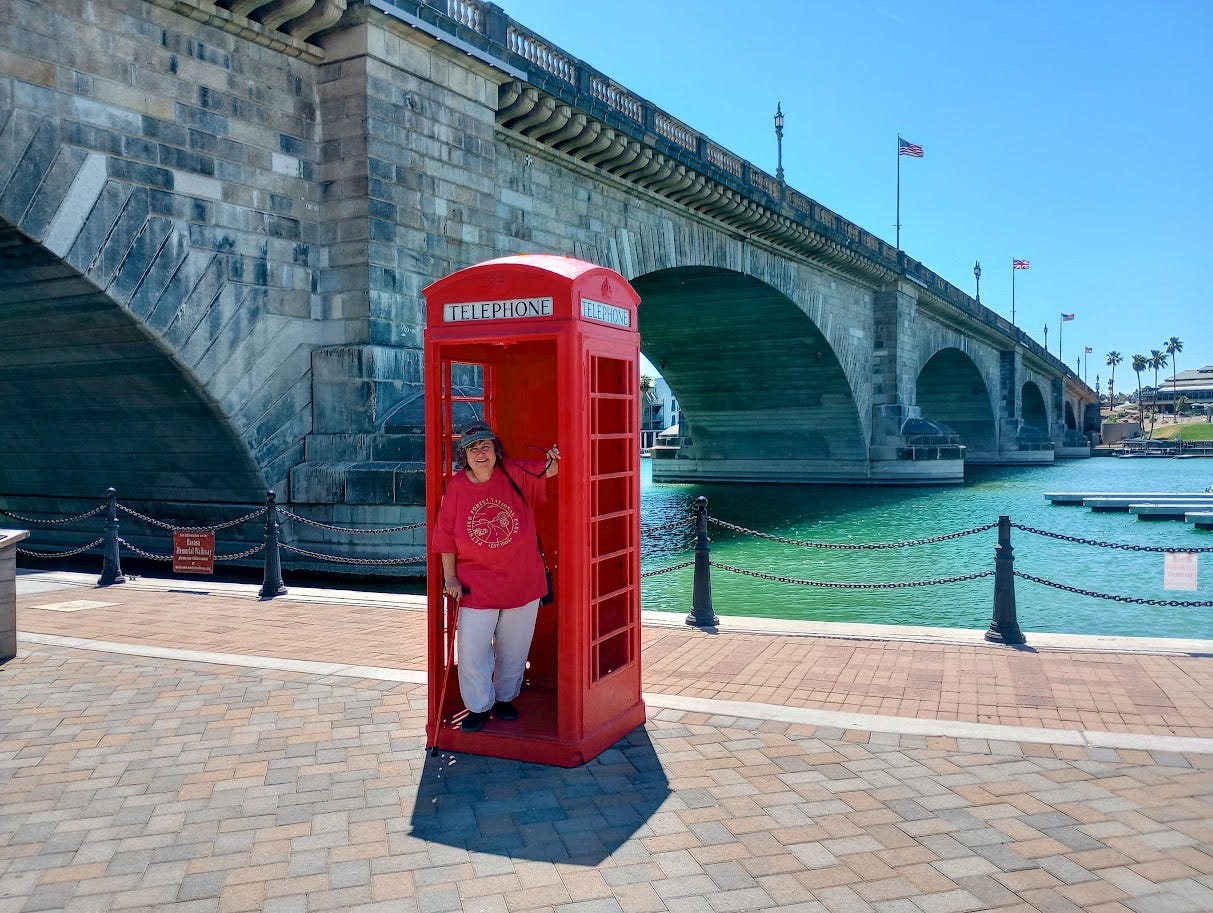 Annette standing in old British phone box in front of large stone bridge over water