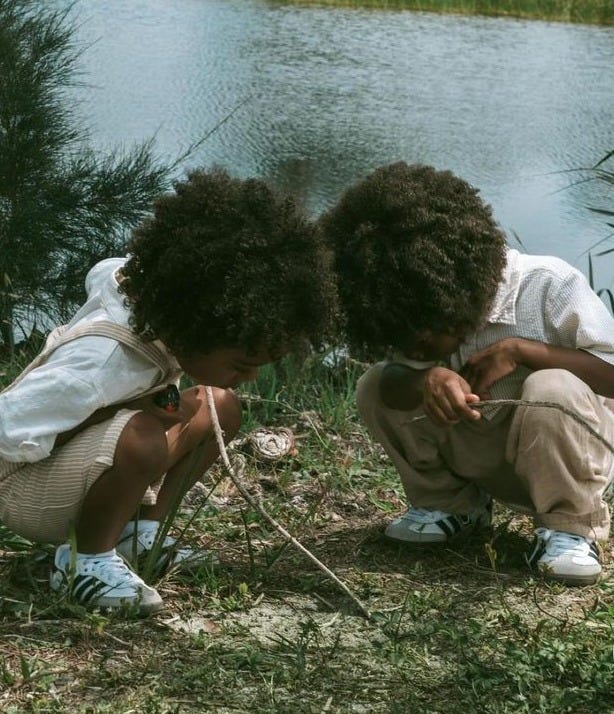 This may contain: two children are sitting on the grass near a lake and looking at something in front of them