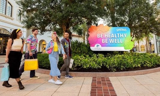 people walking in front of a sign that says be healthy be well
