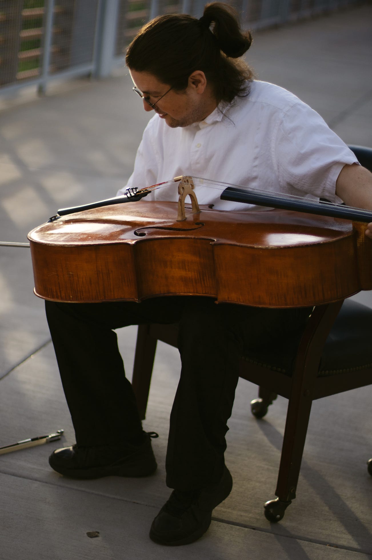 A man with glasses and a white shirt looking over a cello perched on his lap.