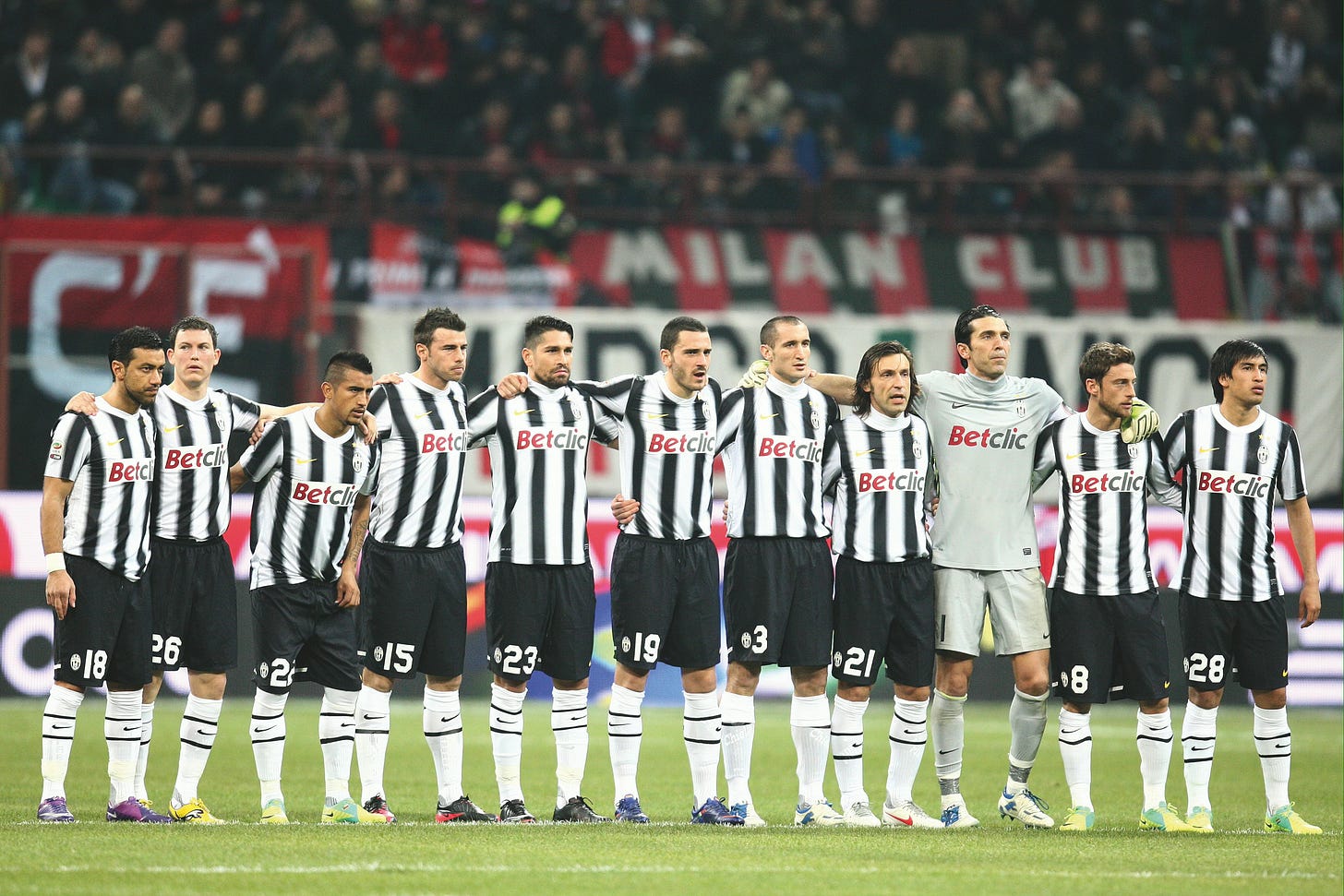 Juventus starting lineup stands arm in arm before kickoff, wearing black and white Betclic-sponsored jerseys during a Serie A match.
