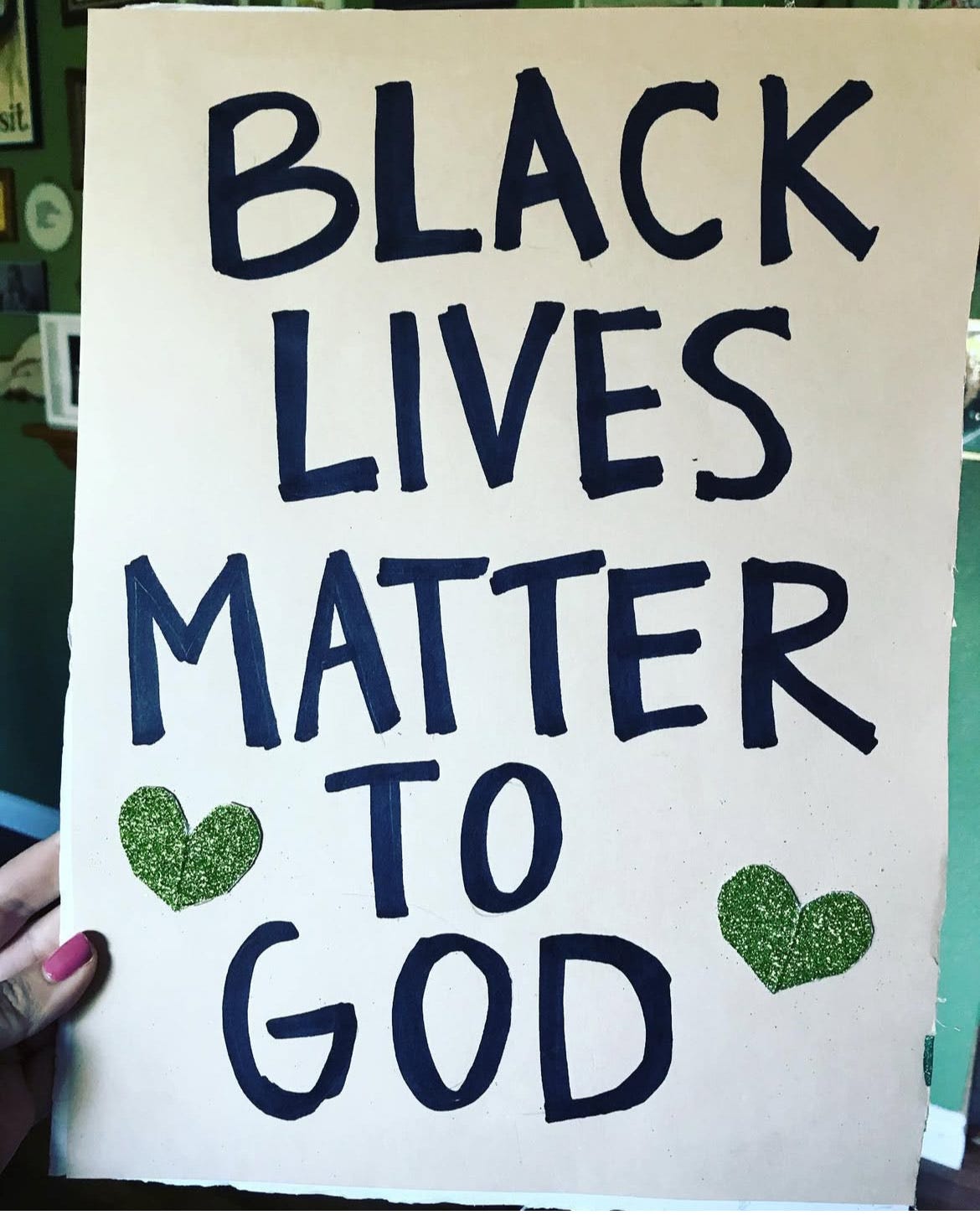 a cardboard sign with big bold letters says black lives matter to god