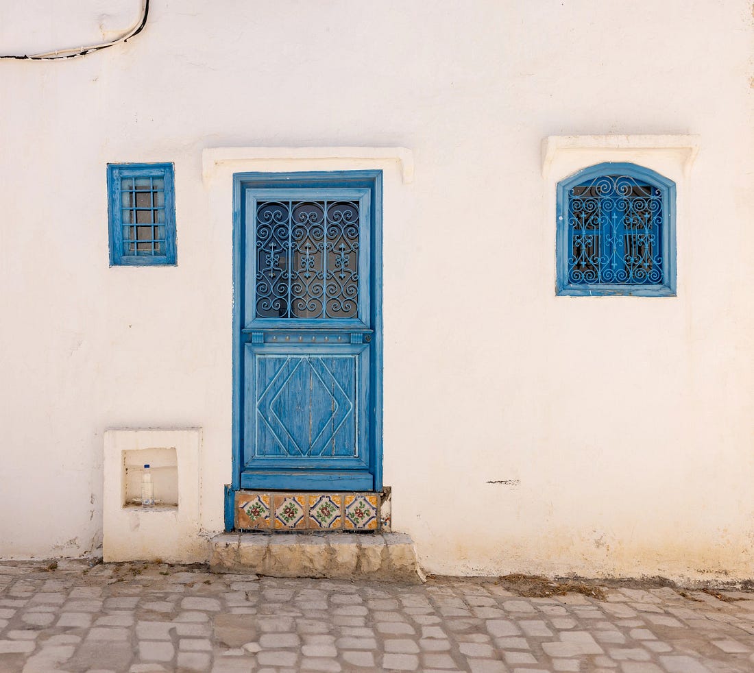 Simple blue-painted door and windows set in a whitewashed wall in Sidi Bou Said, Tunisia. The wrought-iron latticework and hand-painted tiles at the doorstep reflect the quiet craftsmanship and understated harmony that define the village's timeless character. Simple blue-painted door and windows set in a whitewashed wall in Sidi Bou Said, Tunisia. The wrought-iron latticework and hand-painted tiles at the doorstep reflect the quiet craftsmanship and understated harmony that define the village's timeless character.