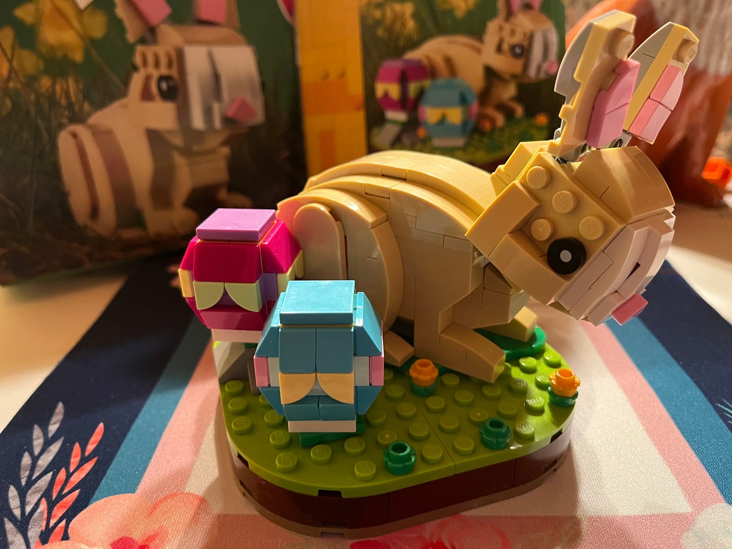 Photo of a small LEGO build of a cute brown bunny next to a couple of Easter eggs on a green base with flowers.