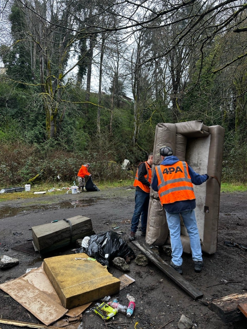 A group of men in orange vests unloading a mattress

Description automatically generated