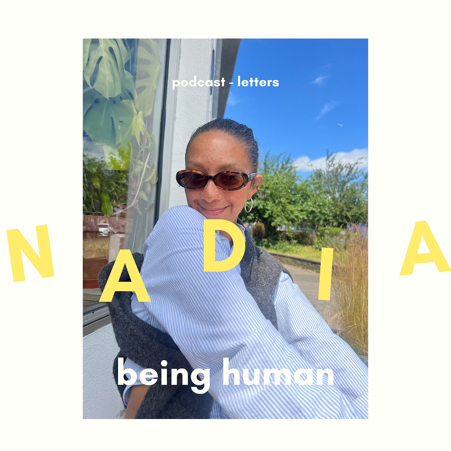 "Nadia sitting outside a cafe under a blue sky, wearing sunglasses by DMY and a striped Ralph Lauren shirt, enjoying a sunny day."