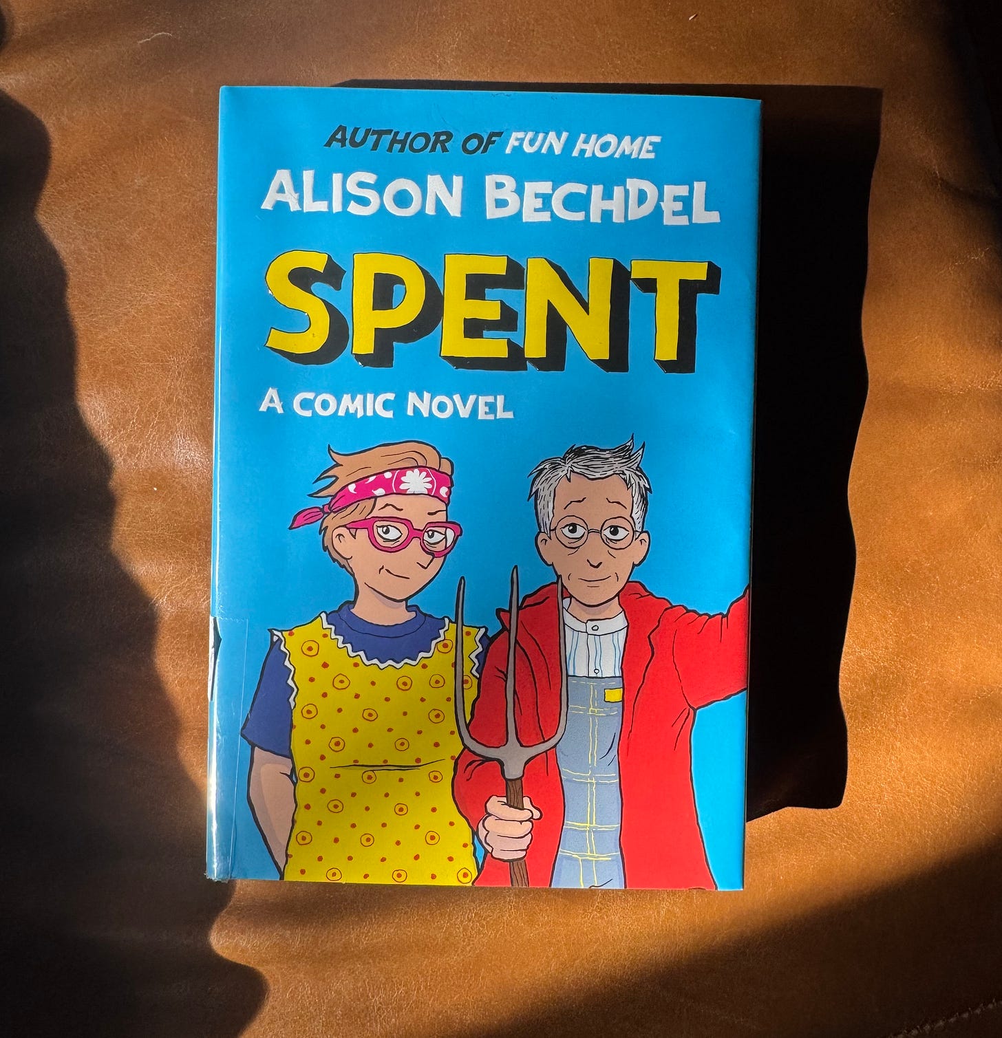 A photo of Alison Bechdel's newest graphic novel Spent: A Comic Novel, with a drawing of two white dykes cast in the familiar pose of American Gothic, with a wry vibe