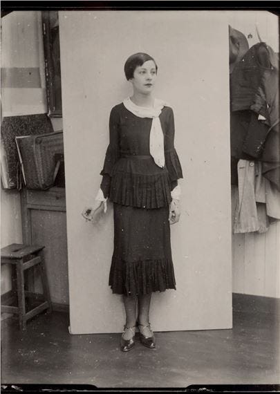 A vintage black-and-white portrait of a woman in a fringed dress standing against a plain backdrop.