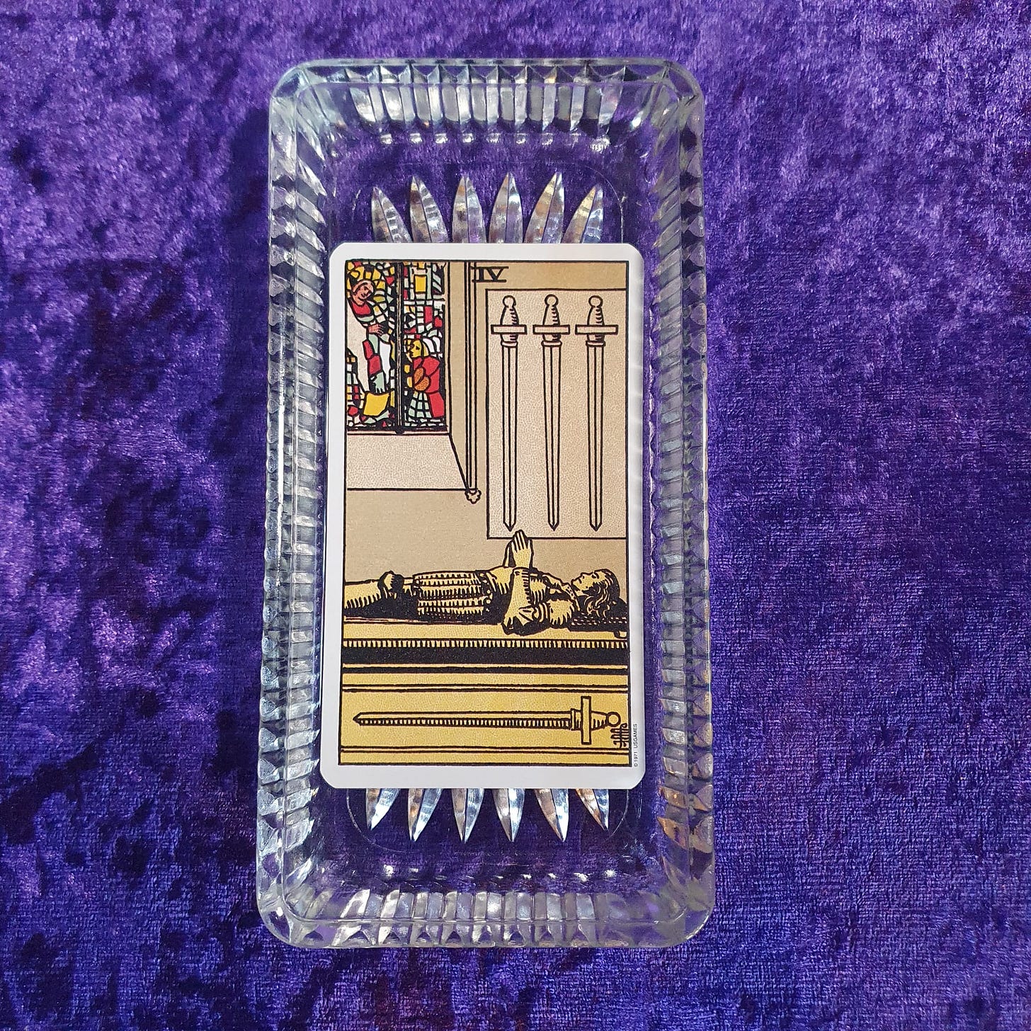 The Four of Swords sits in a glass dish on a purple velvet background The Four of Swords sits in a glass dish on a purple velvet background