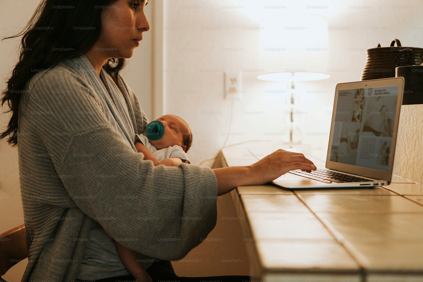 Madre usando una computadora y sosteniendo a su bebé Madre usando una computadora y sosteniendo a su bebé
