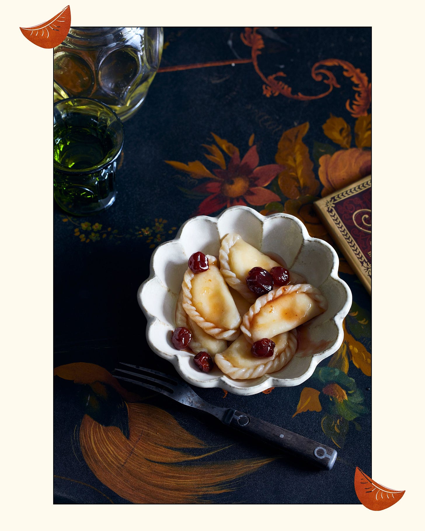 a bowl of cherry-topped varenyky on a table with a dark tablecloth and glasses a bowl of cherry-topped varenyky on a table with a dark tablecloth and glasses