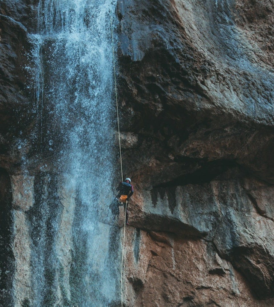 person in blue jacket climbing on rocky mountain during daytime person in blue jacket climbing on rocky mountain during daytime