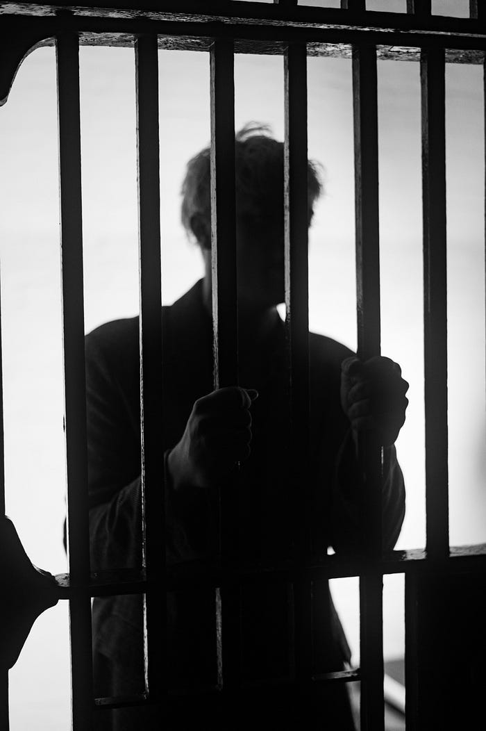 A prisoner’s silhouette in black and white as he clings to the bars of his cell. A prisoner’s silhouette in black and white as he clings to the bars of his cell.