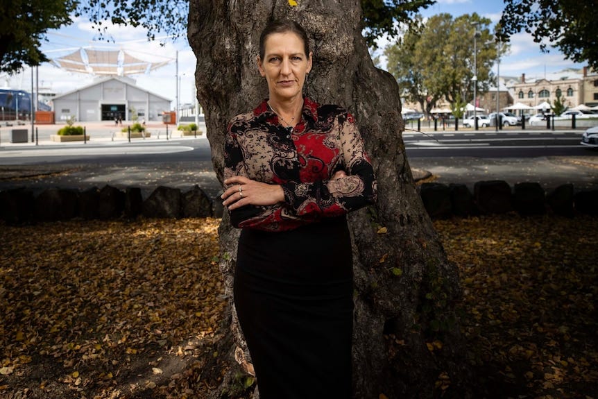 Woman stands with her arms folded in front of a tree. Woman stands with her arms folded in front of a tree.