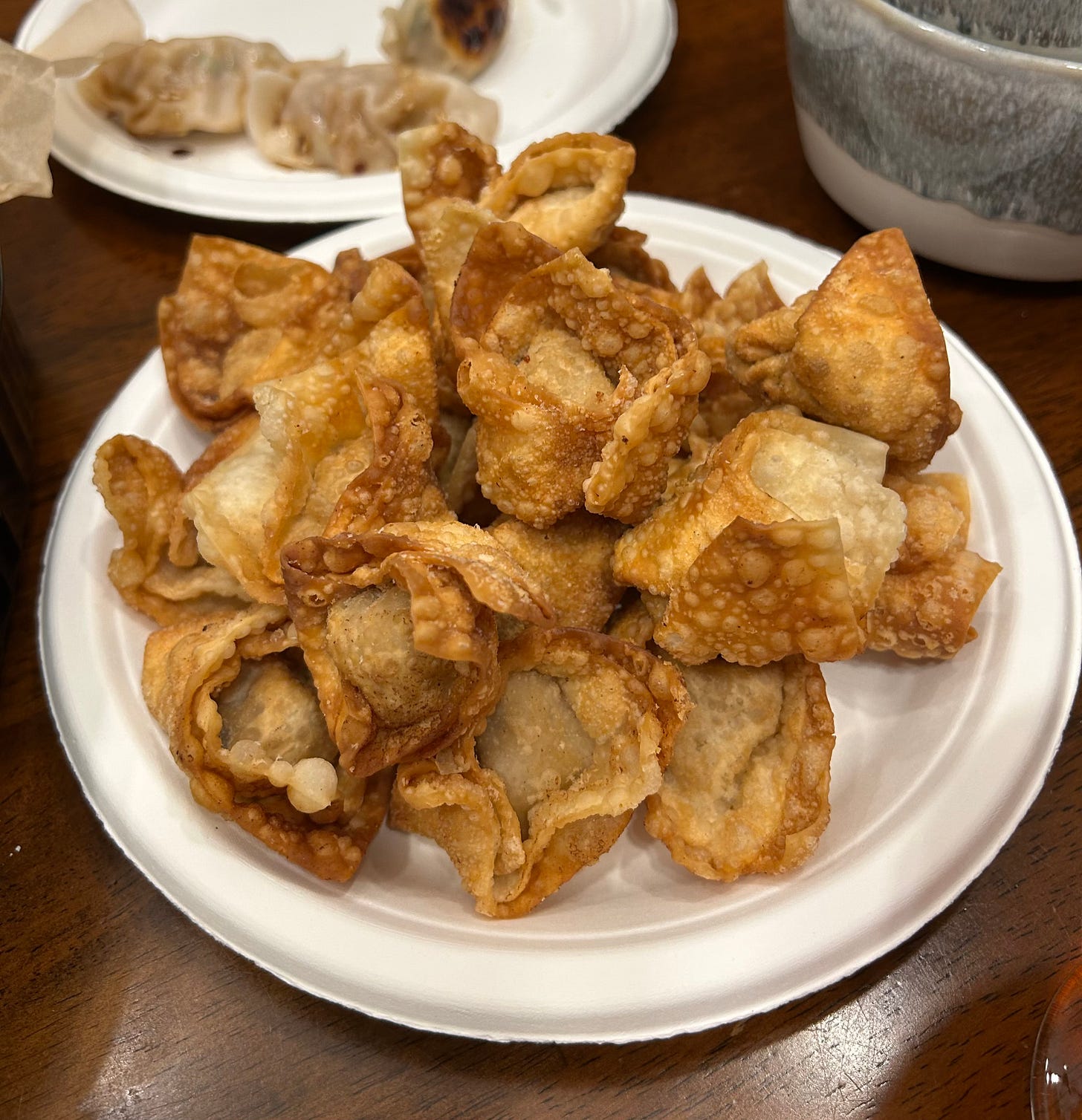 A round plate piled with golden, deep-fried wontons on a wooden table.