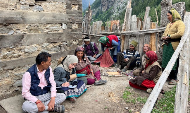 Un chercheur en tenue de terrain partageant une discussion avec un groupe de villageoises en tenue traditionnelle, fichus sur la tête