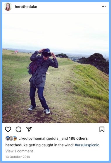 Hero posts an image of Dogberry leaning in the wind, holding his hat on his head. Green grass stretches behind him. Text reads: getting caught in the wind! #ursulaspicnic