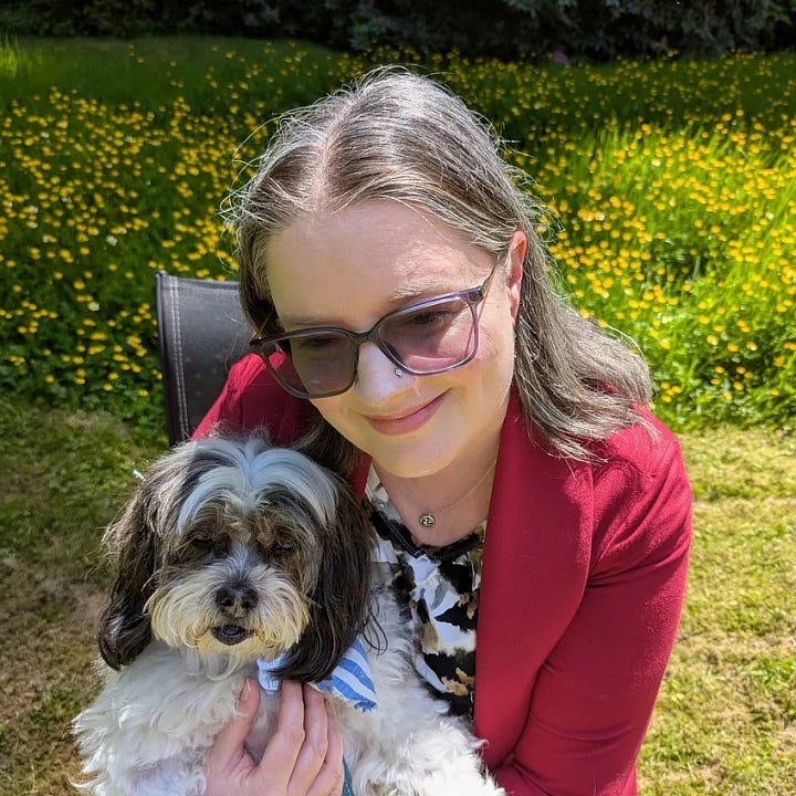 woman in red jacket holds a black and white long haired dog