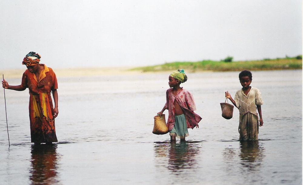A woman and two children wade through water with buckets
