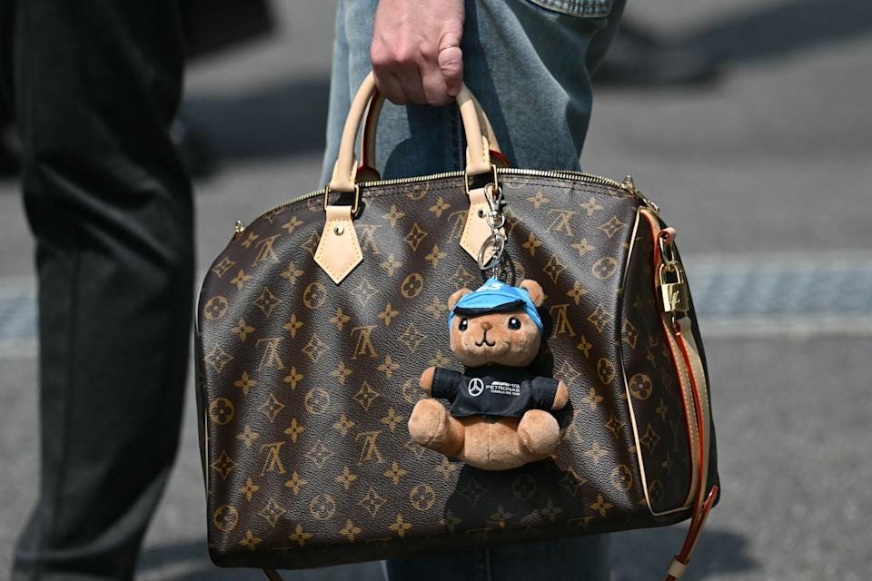 A woman holds a Louis Vuitton bag, seen with a soft toy with the Mercedes logo and the number 63 for Mercedes' British driver George Russel, on race day at the Suzuka circuit during the Formula One Japanese Grand Prix in Suzuka, Mie prefecture on March 29, 2026. (Photo by ANDREW CABALLERO-REYNOLDS / AFP via Getty Images)